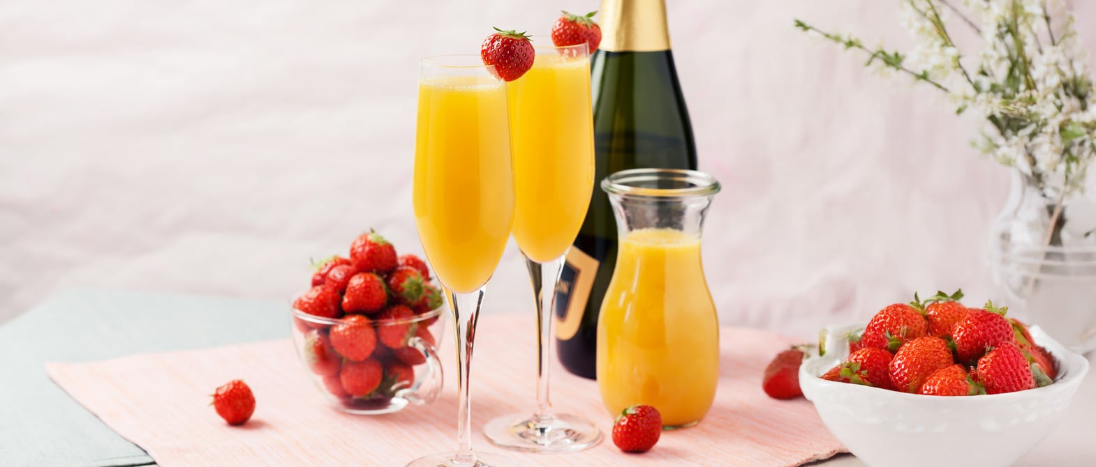 Two bottomless sparkling wine Mimosa brunch cocktails with orange juice and garnished with strawberries